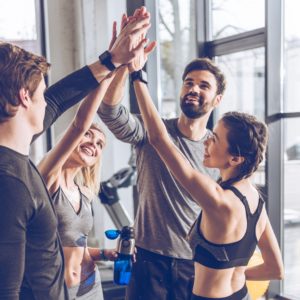 Happy young athletic people in sportswear giving high five in gym